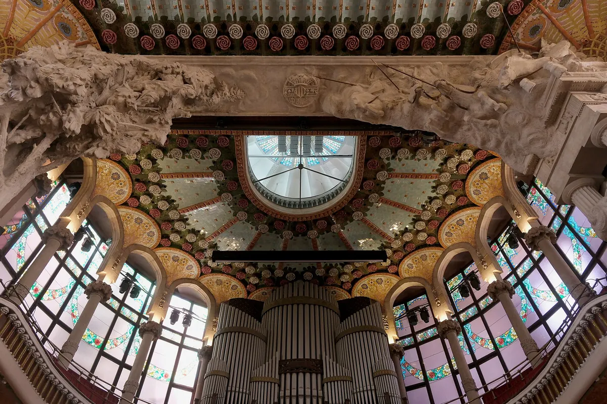 Looking up past the organ to the arch over the stage, with stained-glass windows on both sides and a ceiling of gold and coloured ornament.